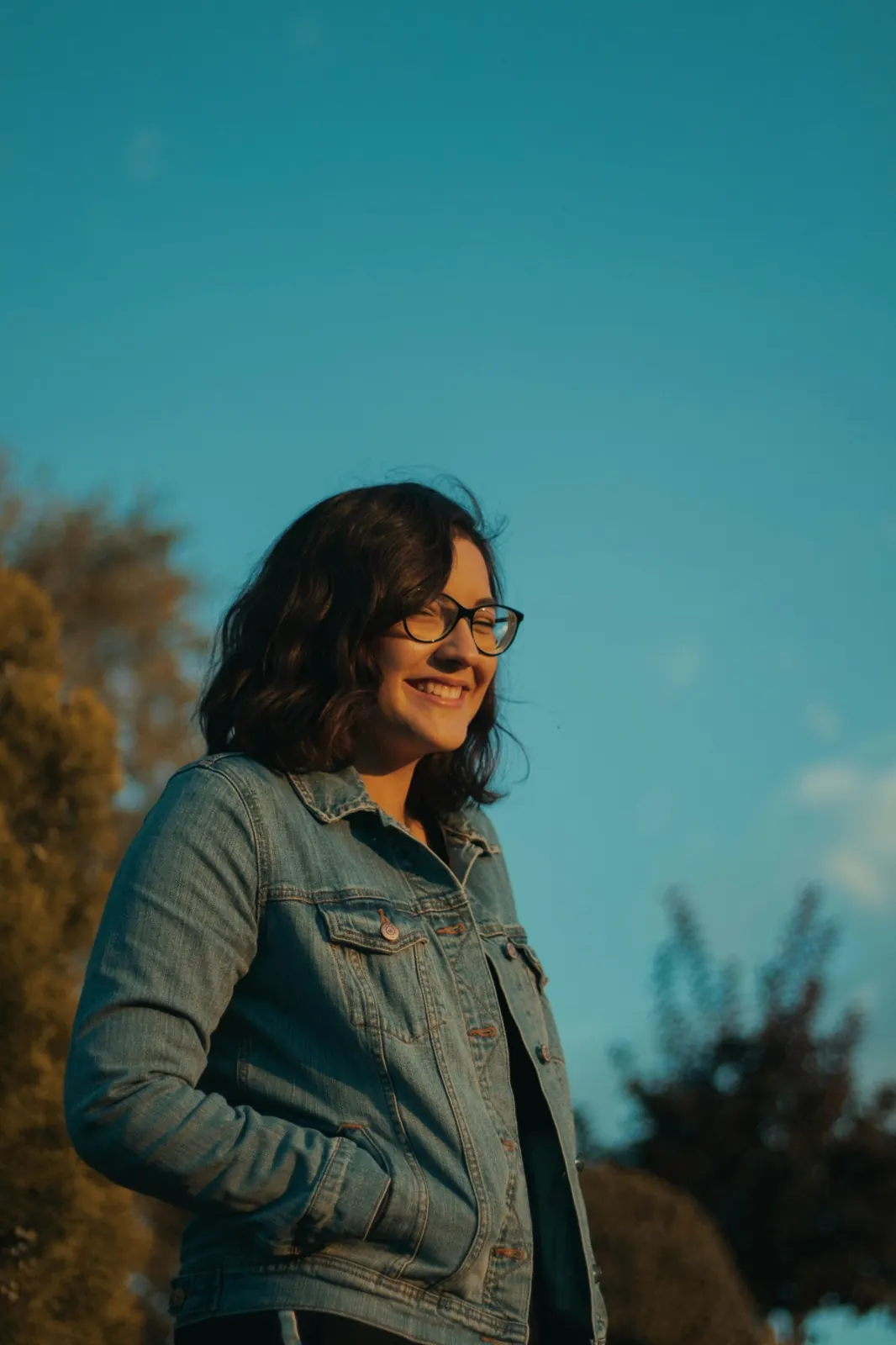 A woman in a denim jacket smiling in warm evening light